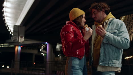 Joyful-couple-kissing-on-urban-street.-Man-and-woman-enjoying-snack-food.