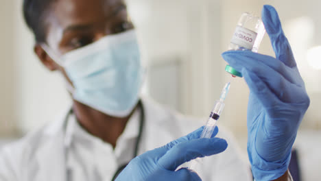 african american female doctor wearing face mask preparing covid vaccine for patient