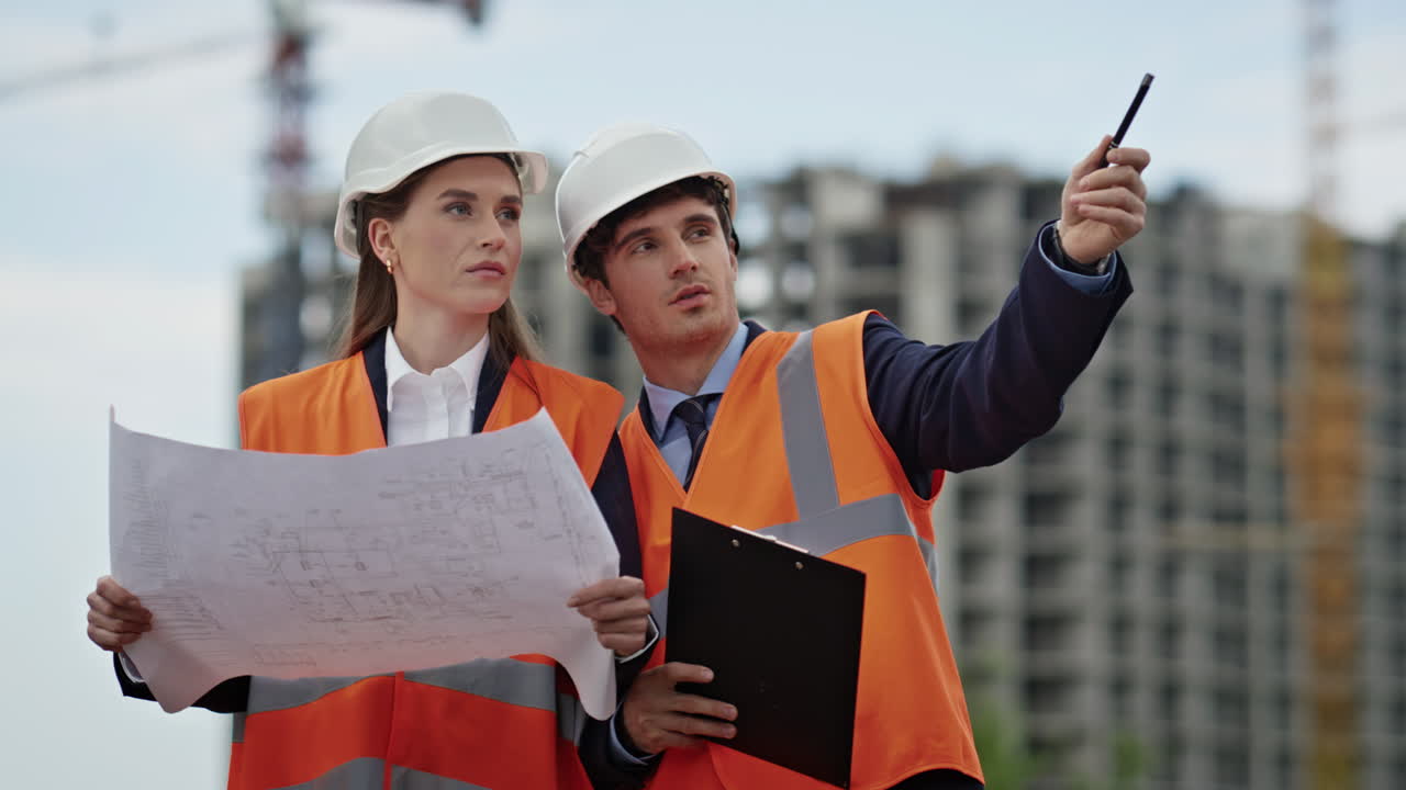 Two engineers examine blueprints discussing project at construction site closeup
