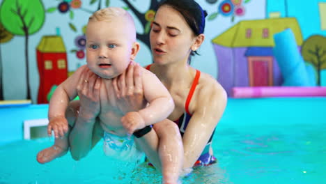 brunette woman dipping a little kid in the water of swimming pool and lifting up. coach is teaching a child to swim.