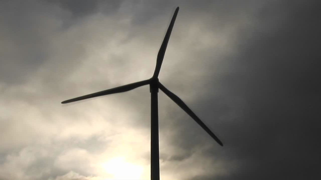 molino de viento retroiluminado genera energía eléctrica en una ladera en california