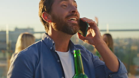 calling guy partying rooftop holding beer bottle closeup. smiling man talking