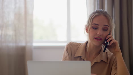 blonde woman talks on phone drinking tea near laptop