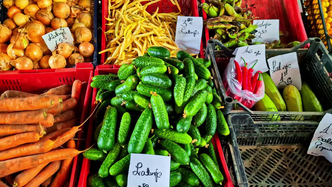 A stand with many different vegetables such as carrots, onions, beans, gherkins and courgettes