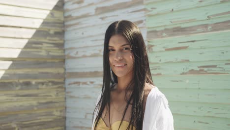 portrait of smiling hispanic woman in front of weathered wooden wall in the sun, slow motion