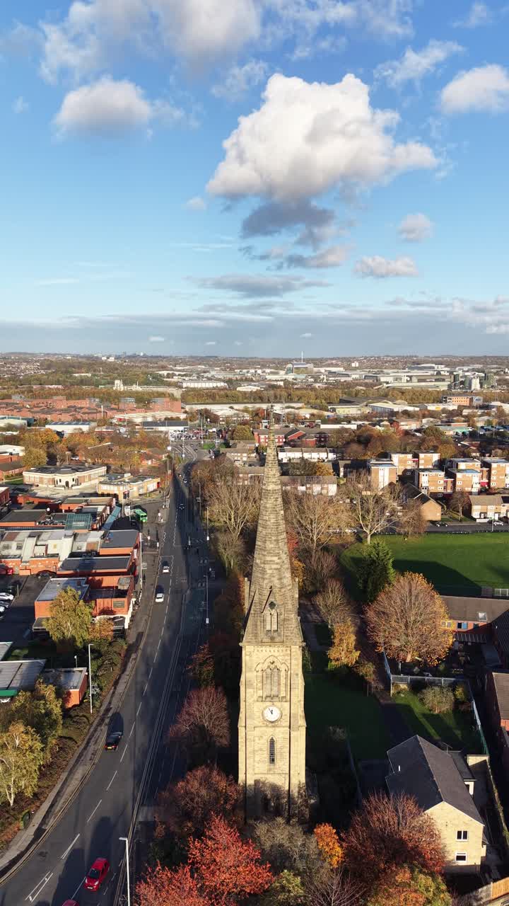 Veduta aerea verticale con drone di Hedge End nell'Hampshire, Inghilterra, con una chiesa storica con un'alta guglia, le strade cittadine circostanti, alberi autunnali, cielo sereno e paesaggio urbano