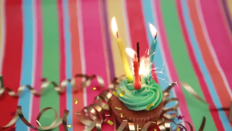 Animation-of-gold-confetti-falling-over-lit-birthday-candles-and-sparkler-in-fairy-cake