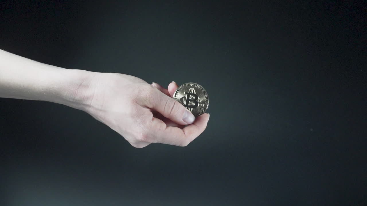 mano que sostiene la moneda de criptomoneda bitcoin brillante, fondo negro