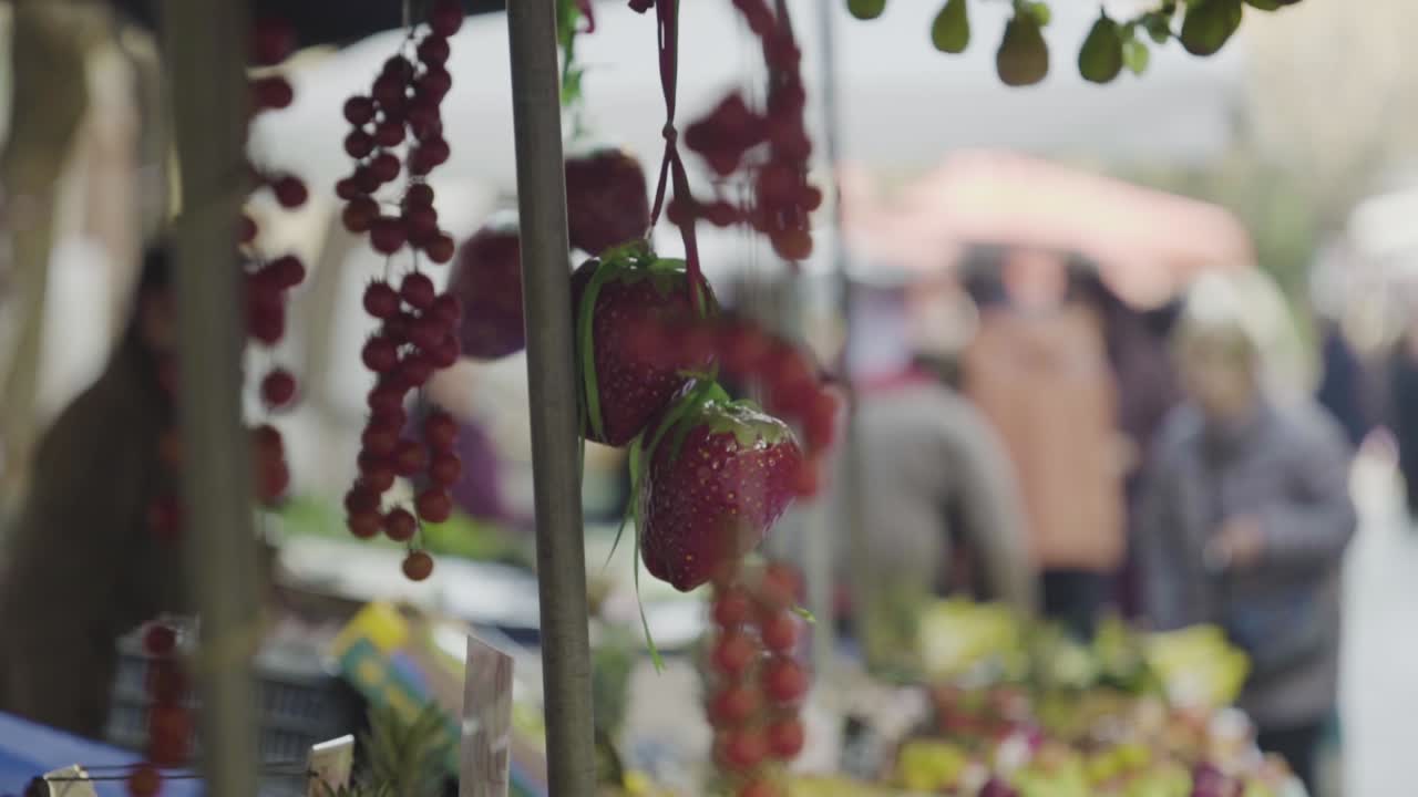 typical day shot at a city street market close up of amazing red strawberries hanging from the tent ready for sell people walkig at background