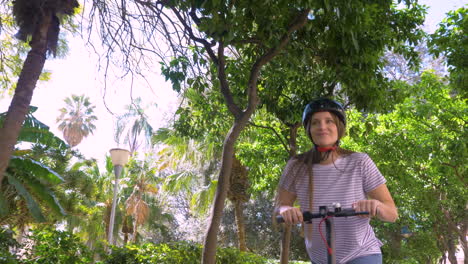 niña feliz montando scooter eléctrico en la ciudad en un día soleado y mirando a la cámara