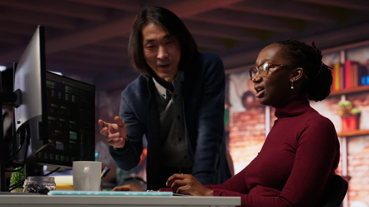 Happy team leader joking with employee doing code testing in relaxed workspace