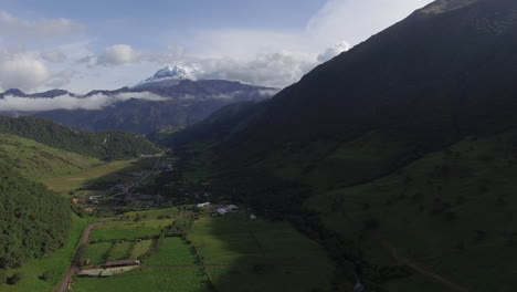 aerial flying through green valley with snow capped mountain in distance