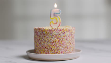 studio shot birthday cake covered with decorations and lit candle celebrating fifth birthday being blown out