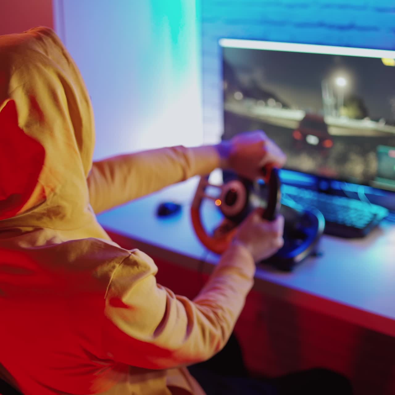 Gamer in orange hood playing video game. Young man enjoys playing car racing with steering wheel at home. Entertainment concept.
