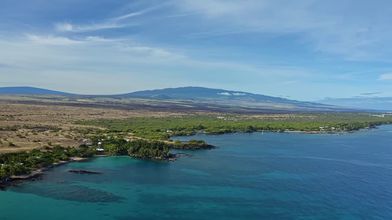 The Hawaiian coast glimmers with turquoise waters against a backdrop of volcanic plains and distant peaks, where ocean and land merge in a breathtaking tropical vista