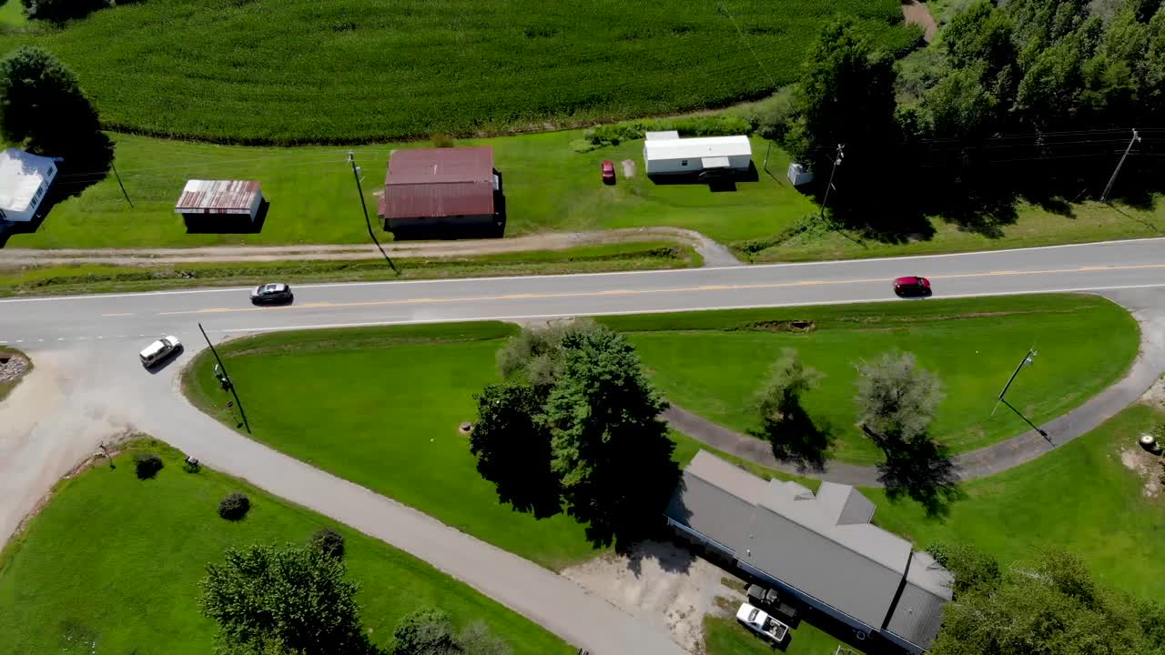 Vista aerea di una strada di campagna con automobili in transito, circondata da campi di mais e alberi in una bella giornata di sole