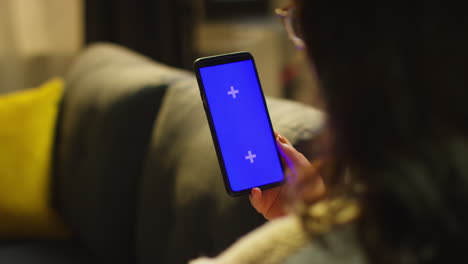 close up over the shoulder shot of woman spending evening at home sitting on sofa looking at blue screen mobile phone 2