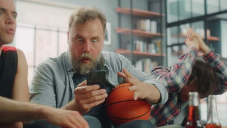 en casa, tres aficionados sentados en el sofá ven el juego de baloncesto en la televisión, usan la aplicación de teléfono inteligente para comprobar la puntuación, la apuesta, las estadísticas, celebran cuando el equipo gana el campeonato.