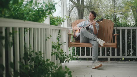 man playing guitar on a porch swing