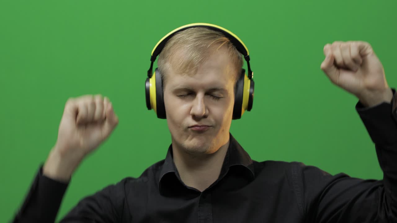 Un homme écoute de la musique avec un casque sans fil jaune et danse. Fond vert