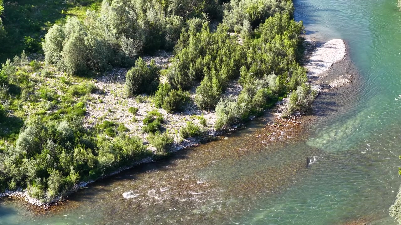 Letecký záběr dronem z výšky zachycuje průzračnou tyrkysovou říční vodu tekoucí podél hustého zeleného lesního břehu.