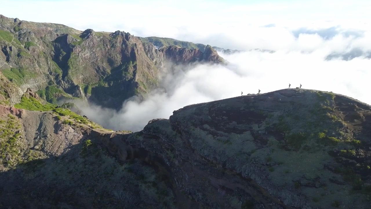 Splendida ripresa aerea con drone di uno stretto sentiero escursionistico su cresta di montagna a Madeira, Portogallo. Caratterizzata da drammatiche cime di roccia vulcanica sopra un immenso mare di nuvole bianche che riempiono la profonda valle sottostante.