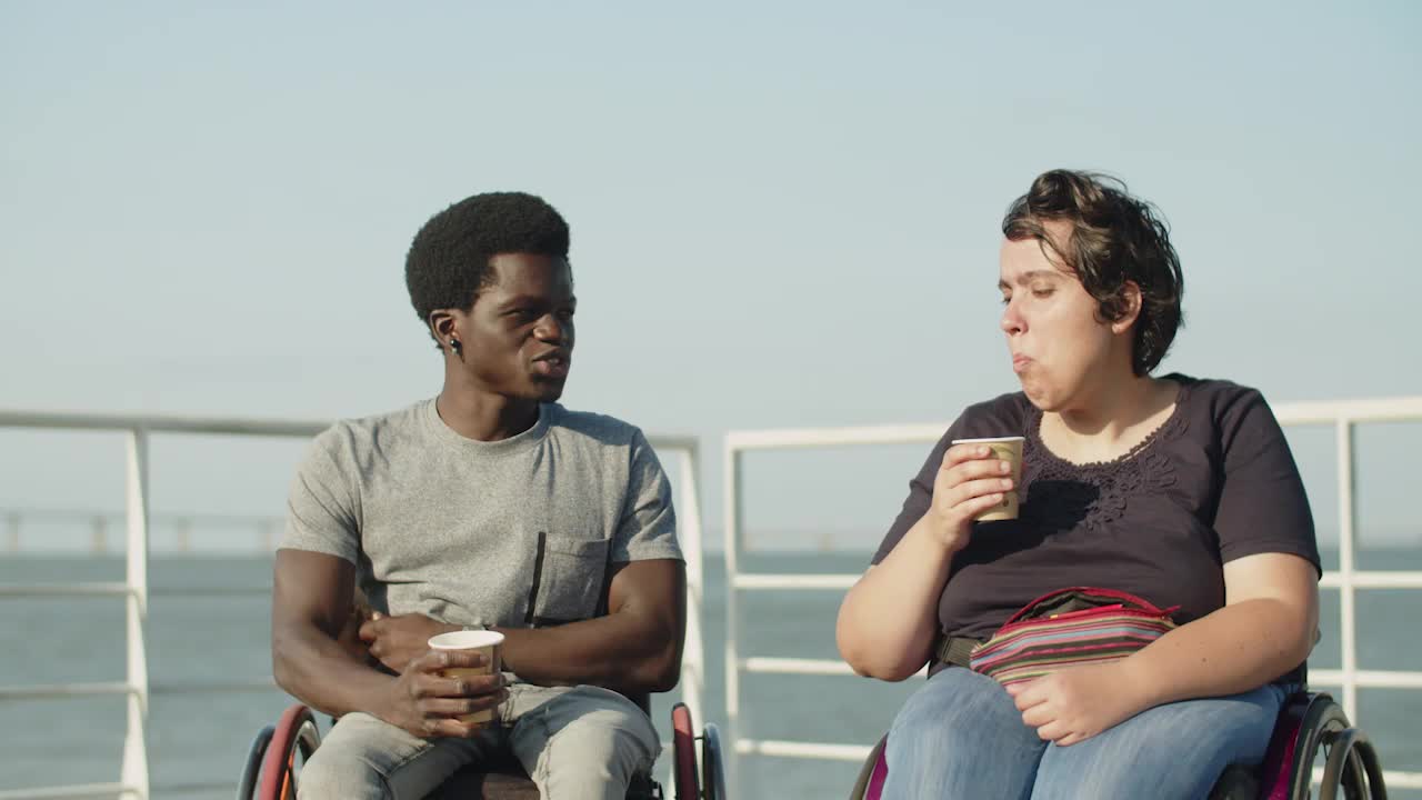 pareja feliz usando sillas de ruedas bebiendo café en el muelle