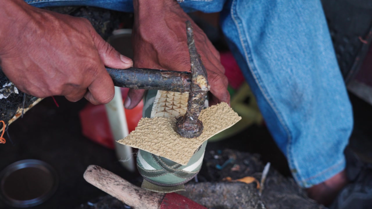 Close-up of a street cobbler hammering a shoe sole during repair in Malaysia, showing precise manual work, traditional tools, and the process of fixing worn footwear. UHD.