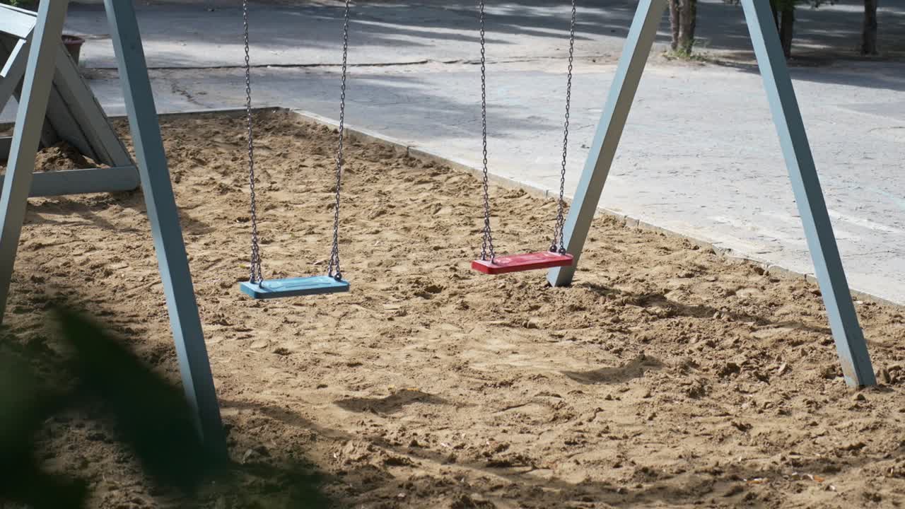 primer plano de dos columpios vacíos colgando sobre una caja de arena en un parque