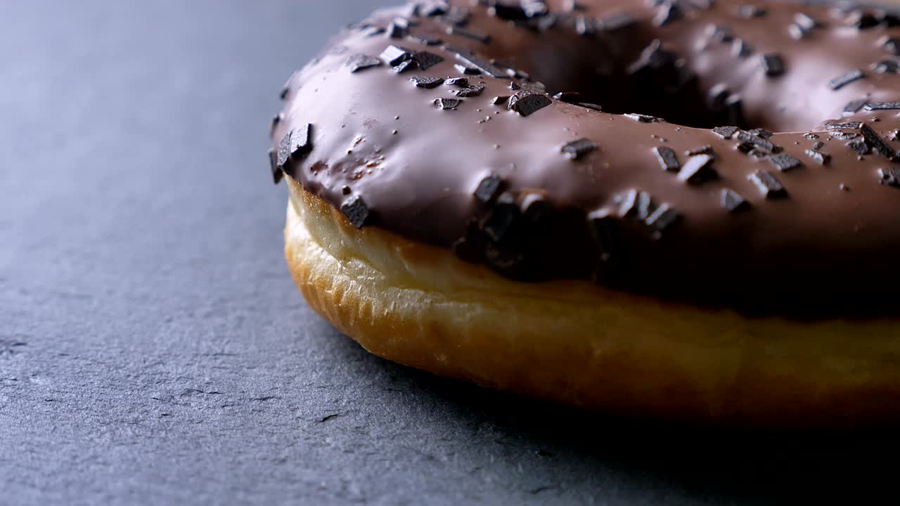 un primer plano de una rosquilla marrón con trozos de chocolate girando lentamente sobre el fondo gris de la mesa.
