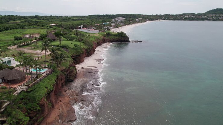 Il drone vola parallelo alla costa verde incontaminata di Careyeros Beach, con la terra a sinistra e il mare a destra.