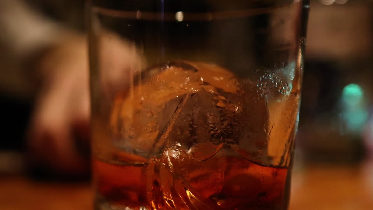 Un primo piano macro dettagliato di una sfera di ghiaccio rotonda all'interno di un bicchiere di cocktail whiskey