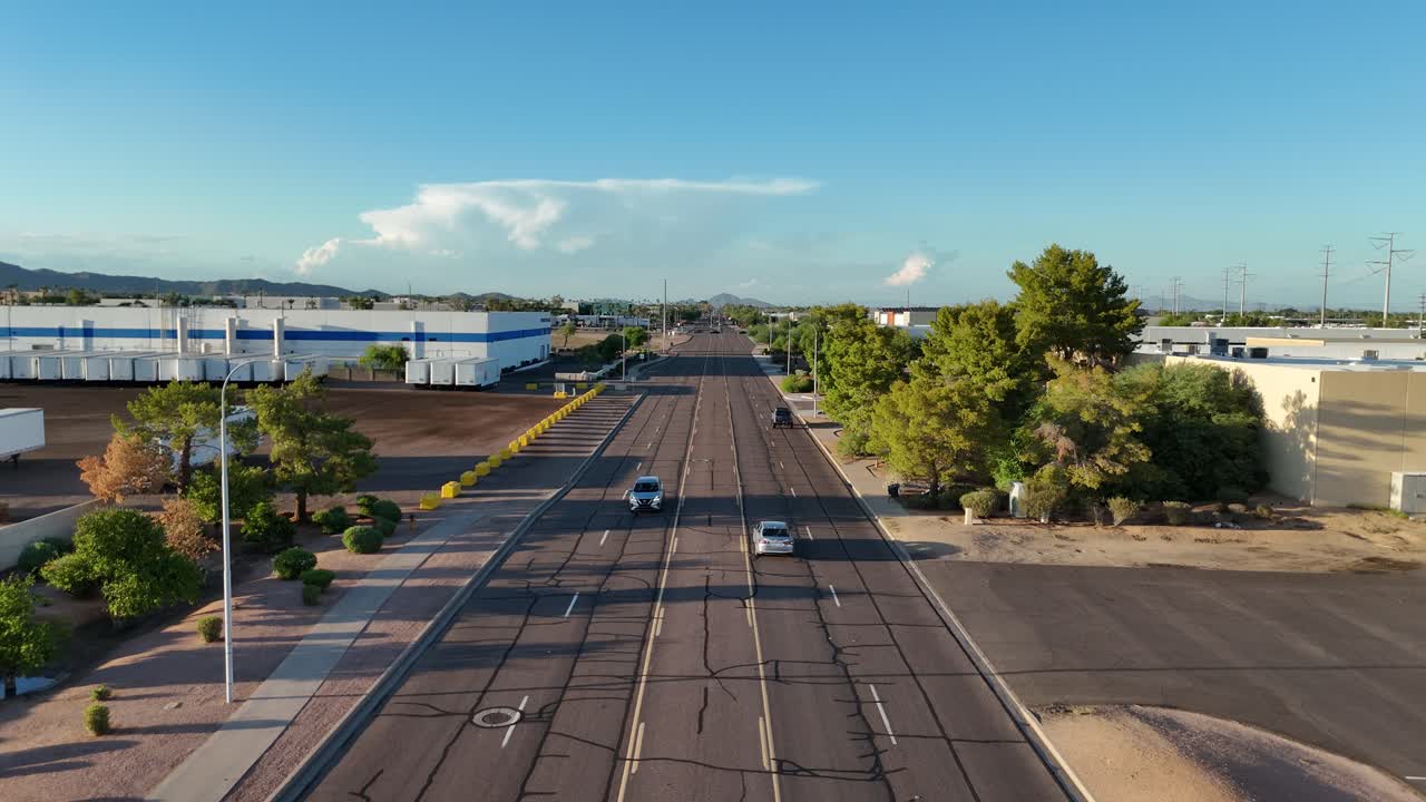 Static Shot of Cars driving down Empty Road with trees on one side and buildings on other side, late afternoon, North 56th Street in Chandler Arizona, Camelback Mountain in the far background