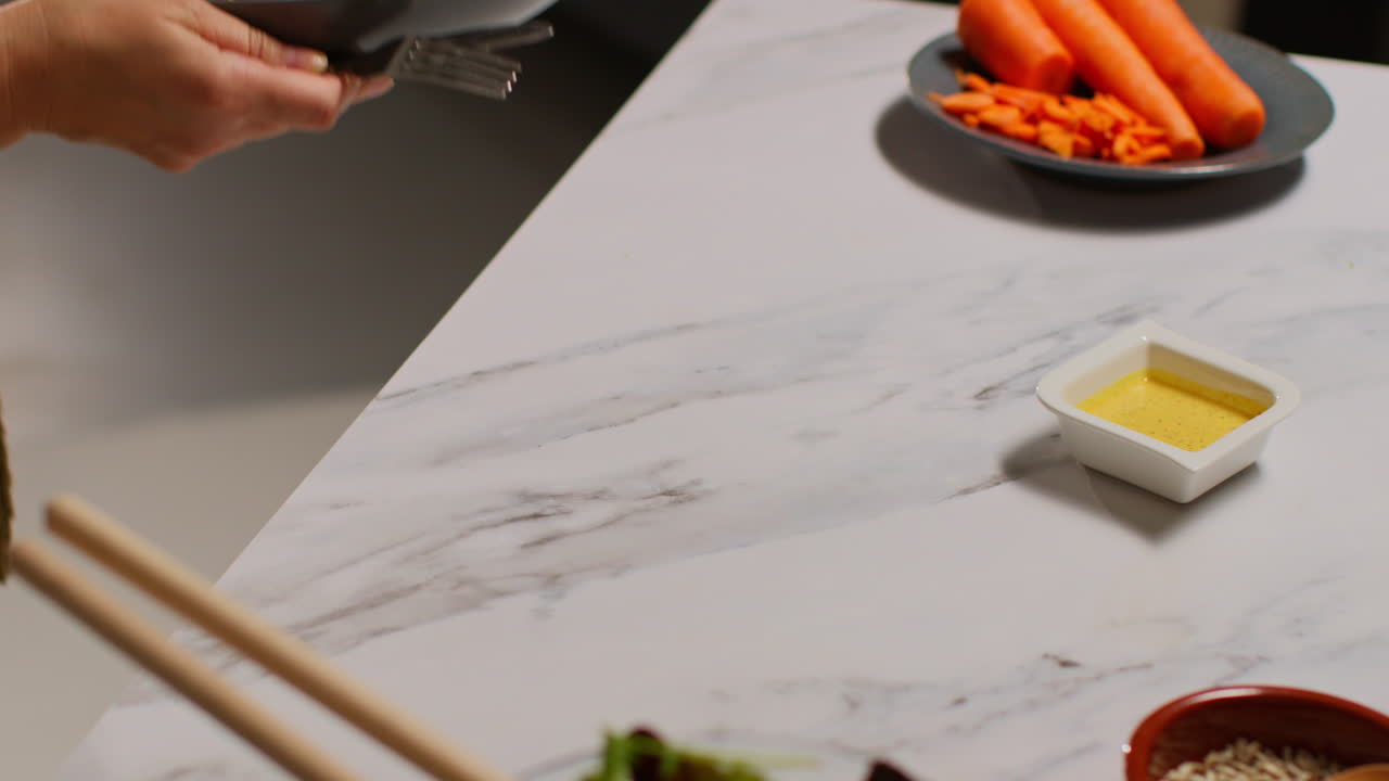 близкий взгляд на женщину дома на кухне, готовящую здоровую вегетарианскую или веганскую еду, съедающую миску салатных листьев с семенами и соусом