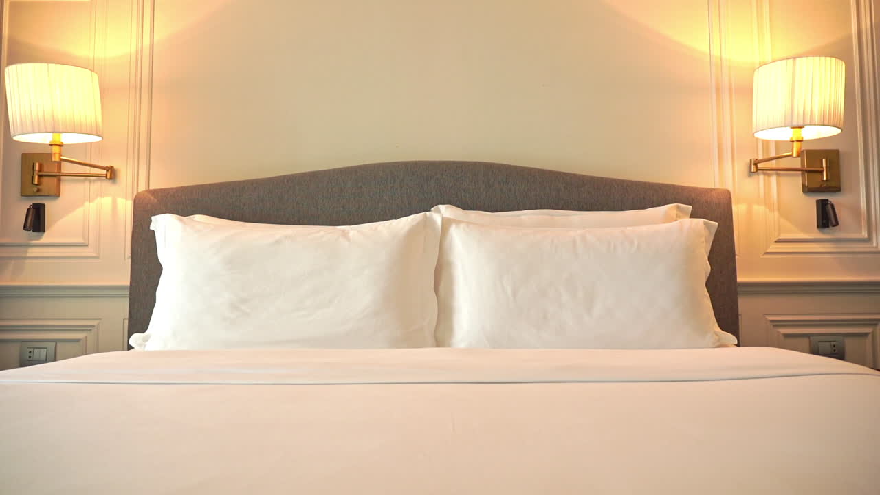 imagen inclinada hacia abajo de una moderna cama doble de hotel recién hecha con mantas y sábanas blancas y un juego de cuatro almohadas en un diseño interior de habitación color beige crema y blanco