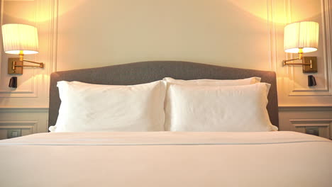 tilt down shot of a modern freshly made resort hotel double bed with white blankets and bedsheets and a set of four pillows in a beige creme white room interior design