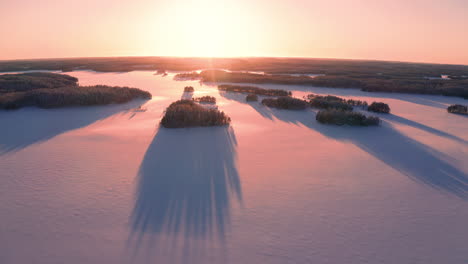 aerial drone shot of sunset over untouched icy lake with long shadows of small islands