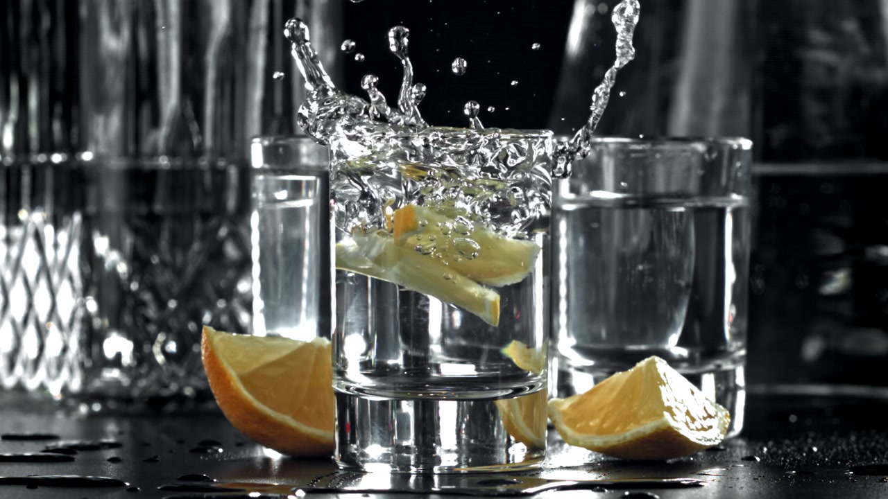 Movimento rallentato di una fetta di limone che cade in un bicchierino con uno schizzo.