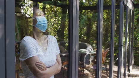 mujer asiática con máscara facial y mirando por la ventana