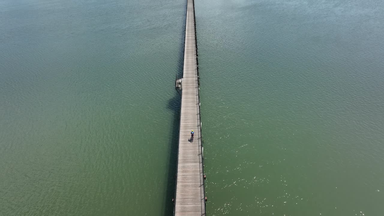 toma aérea de un ciclista cabalgando sobre un largo muelle de madera