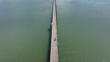 overhead aerial shot of a biker riding on a long wooden pier