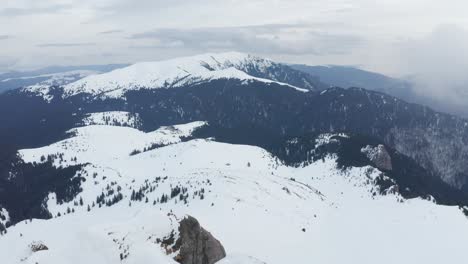 Snow-covered-Ciucas-Mountains-under-cloudy-skies,-serene-and-untouched-landscape,-daylight-shot,-aerial-view