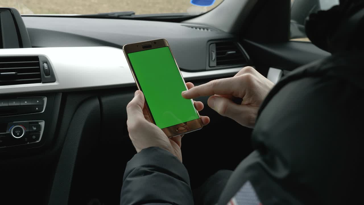 hombre de pantalla verde sosteniendo su teléfono inteligente en un coche
