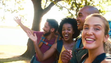 group of friends with backpacks posing for selfie on mobile phone on vacation hiking in countryside