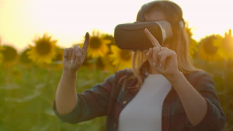 the female is working in vr glasses. she is engaged in the working process. it is a perfect sunny day in the sunflower field.