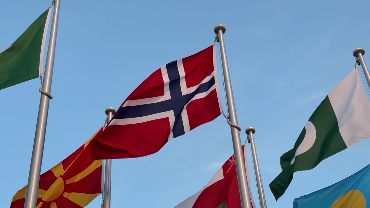 The Norwegian flag flutters gracefully in the breeze under a clear blue sky, symbolizing Norway’s heritage, unity, and presence on the global stage