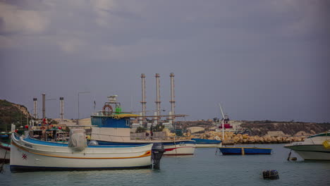 pequeños barcos privados amarrados cerca de la costa de malta con edificios industriales en el fondo
