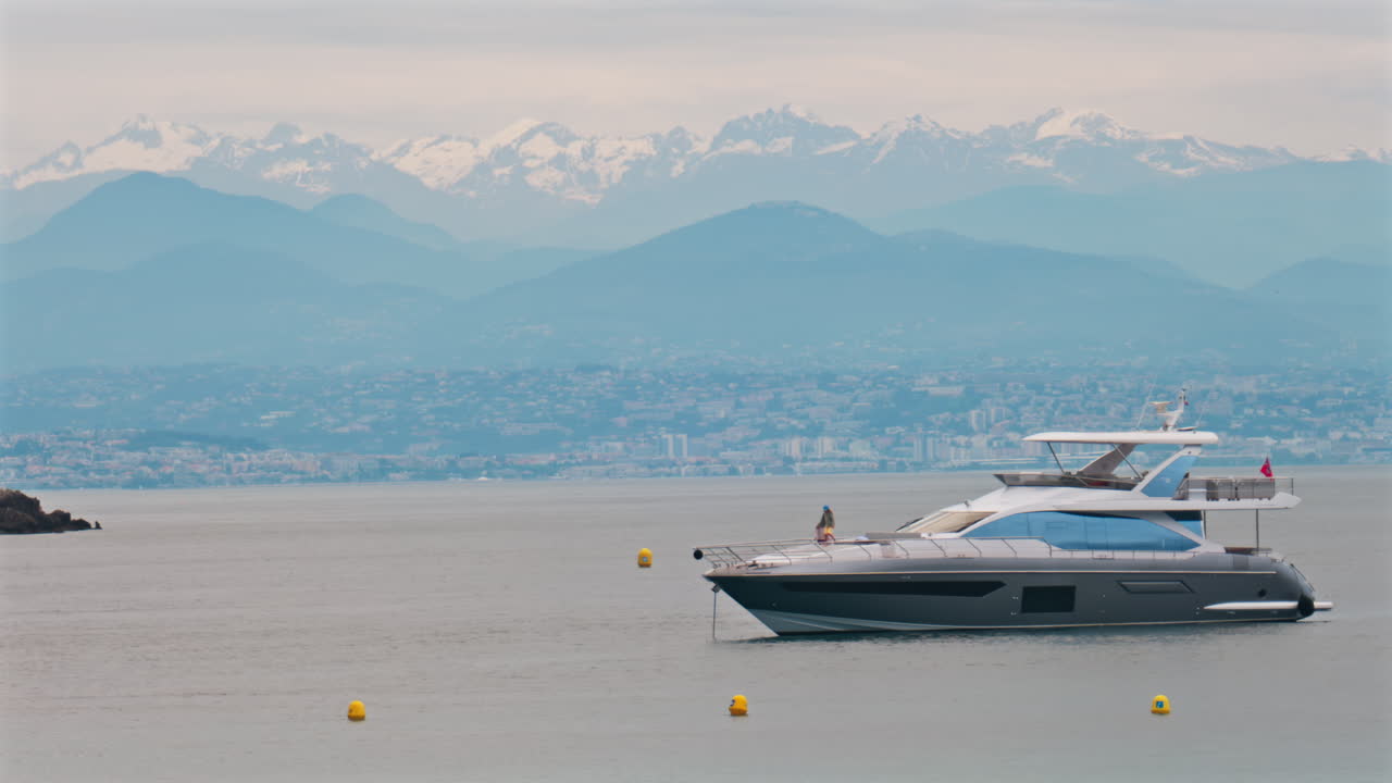 Antibes, France - May 6, 2025: People on a boat docked on the sea with the city and mountains on the background in daylight