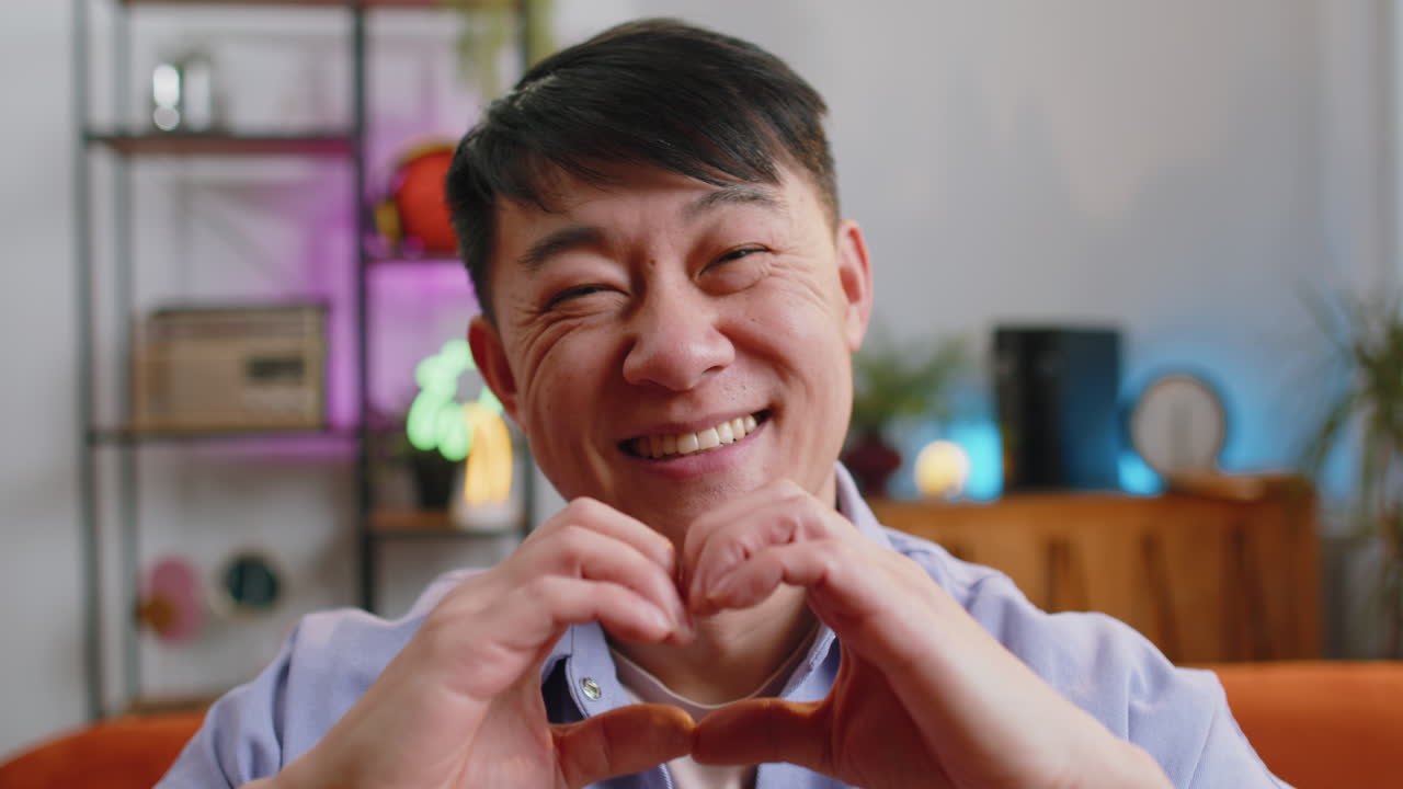 Happy asian man guy makes symbol of love showing heart sign to camera express romantic feelings