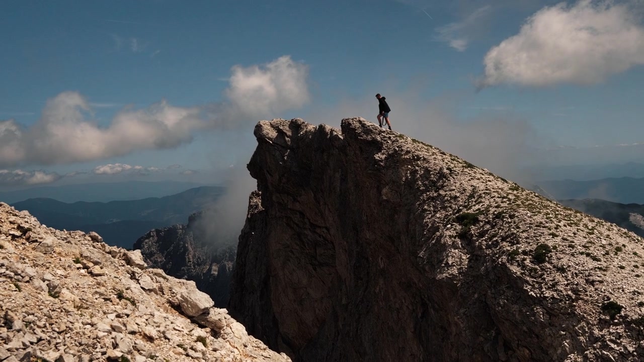 Solo hiker walks toward a dramatic rocky mountain peak under a blue sky. Outdoor adventure scene showing hiking, achievement and reaching the summit.